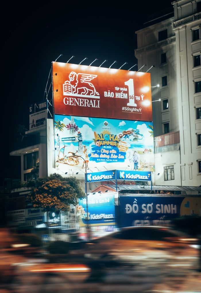Oferty Blurred motion captures a bustling urban street at night with bright billboards.