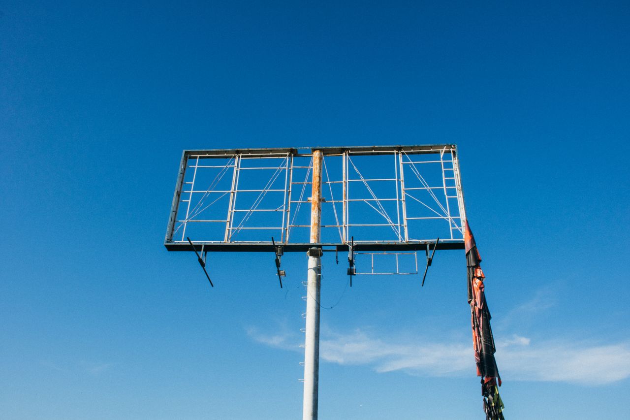 The Art of Drawing Readers In: Your attractive post title goes here A rusty, empty billboard frame stands against a vast clear blue sky, symbolizing abandonment.